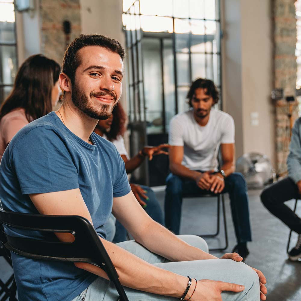 a man sits in a support group circle smiling