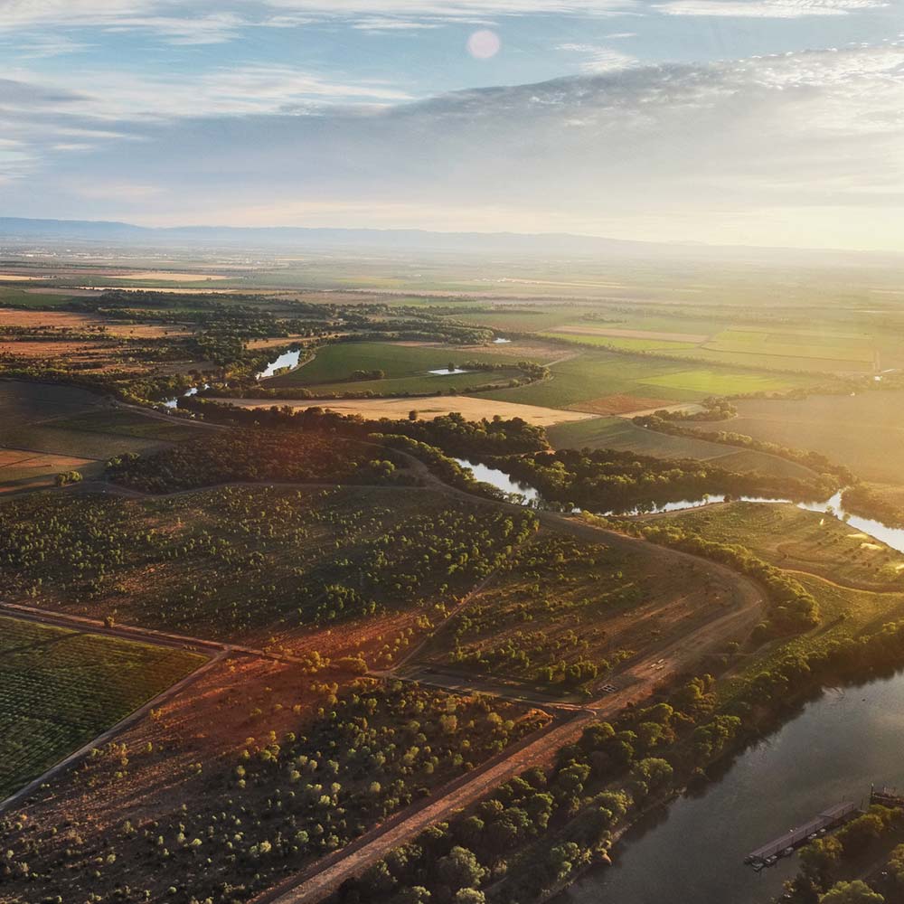 an evening sunset casts its warm glow over a patchwork of farm fields and a river winding its way through the land